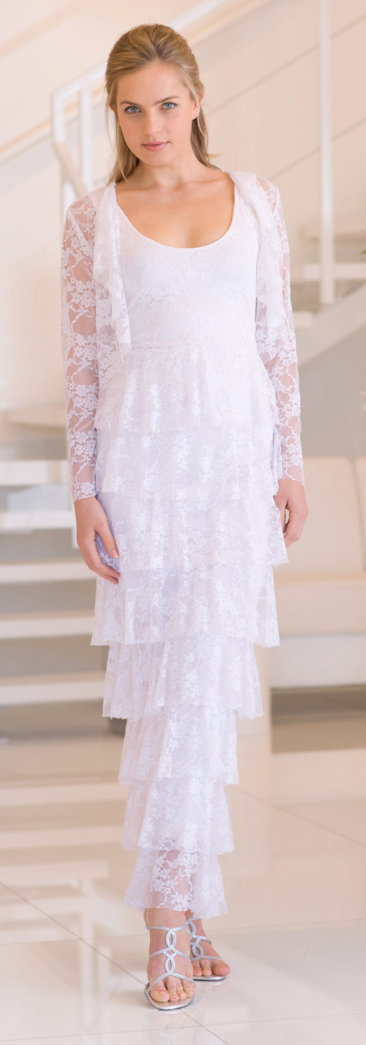Woman wearing a long white lace dress in a bright room.