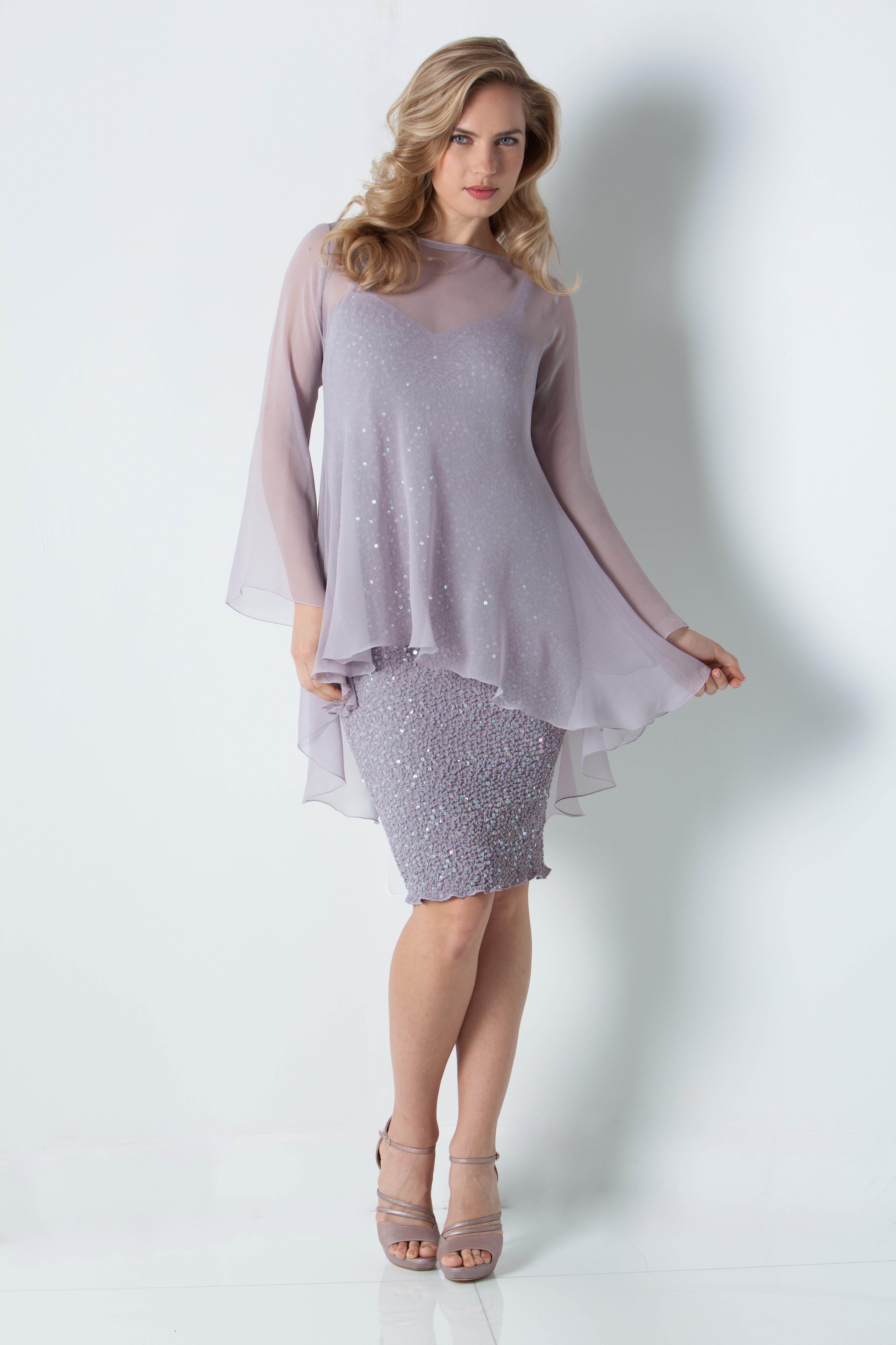 Woman wearing a light stone color dress with a sheer overlay on a white background
