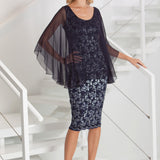 Woman wearing a dark blue silver lace dress with sheer overlay on a white staircase.