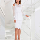 Woman wearing a white lace two-piece outfit standing in a white geometric room.