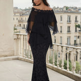 Woman wearing a black layered off the shoulder blouse with a long lace mermaid skirt on a balcony