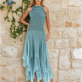 Woman in a Sequin Halter Top Dress  by a stone wall adorned with green vines and purple flowers.