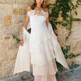 Woman wearing a strapless dress with a  sequin bodice and a silk stole against a stone background with greenery