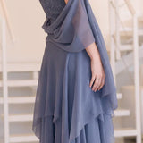 Woman wearing ruffle neck sequin halter dress with layered silk hem and stole in front of modern stairway