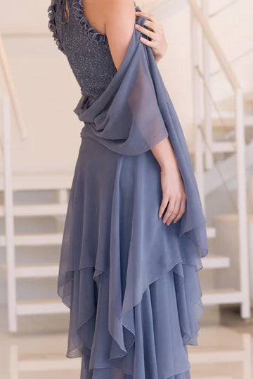 Woman wearing ruffle neck sequin halter dress with layered silk hem and stole in front of modern stairway