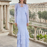 Woman in a light english violet dress standing on a balcony with a cityscape in the background