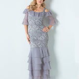 Woman standing in a gray and silver long dress standing in front of a white wall