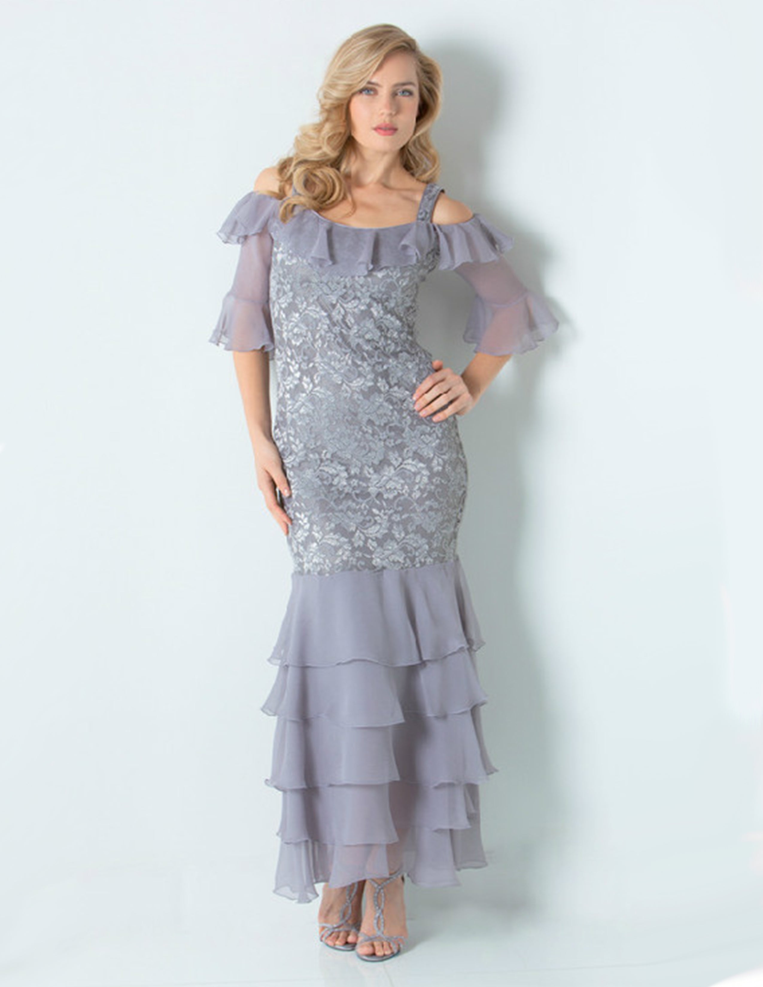 Woman standing in a gray and silver long dress standing in front of a white wall