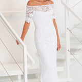 Woman wearing a white lace off-shoulder dress in a minimalistic setting.
