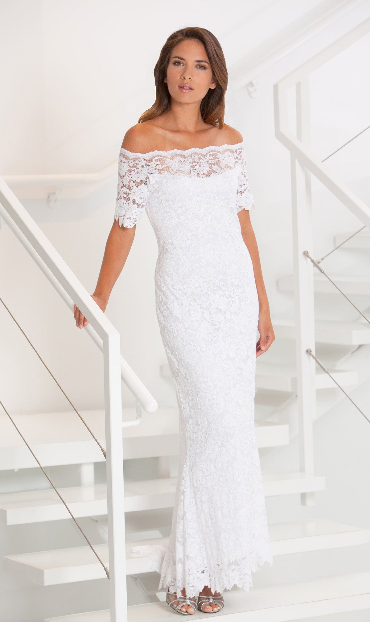 Woman wearing a white lace off-shoulder dress in a minimalistic setting.