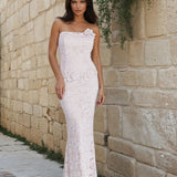Woman in a white lace dress standing against a stone wall.