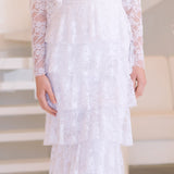 Woman wearing a long white lace dress in a bright room.