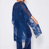 Woman models the Sara Mique Evening Wear Devore Duster Pant Set K1809H/Cami/P1703 in sheer indigo over matching pants and heels, standing sideways and looking over her shoulder against a white background.