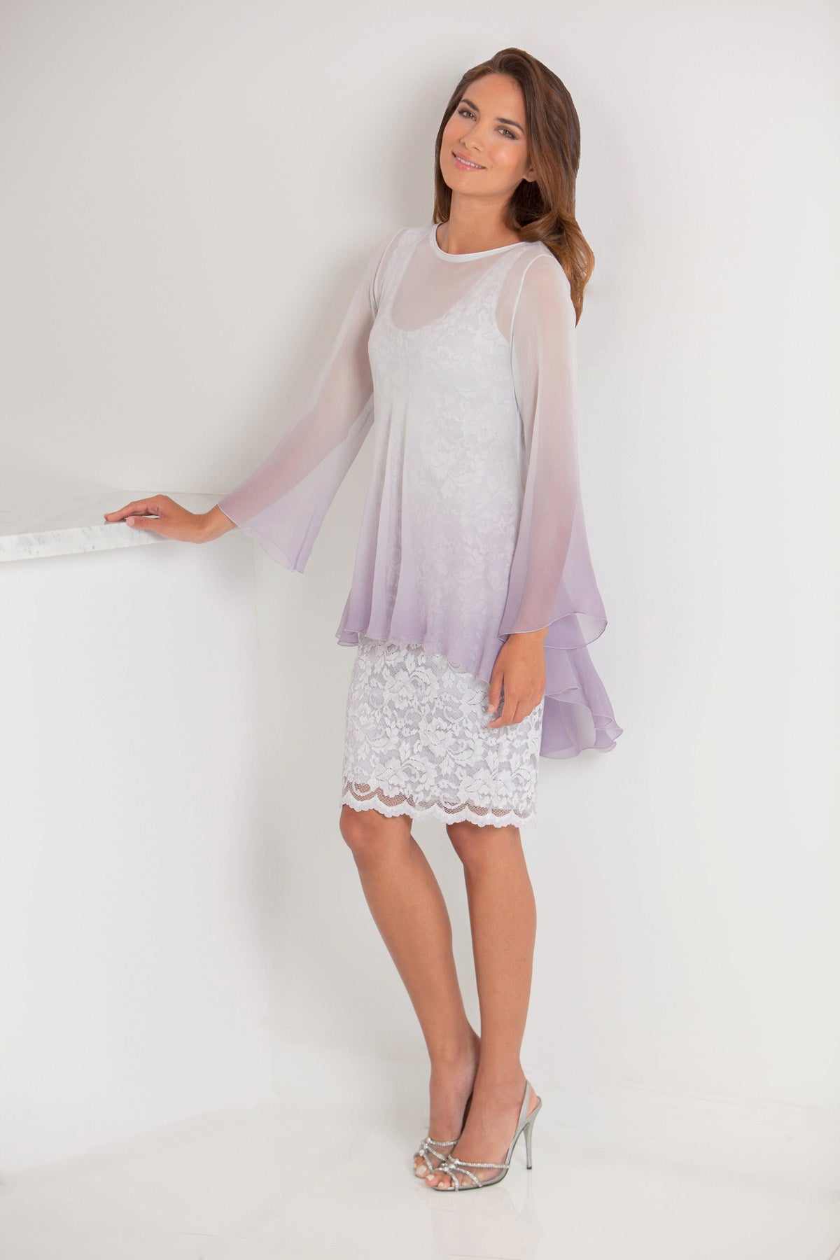 Woman wearing a light orchid top and orchid lace dress against a white background