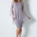 Woman wearing a light stone color dress with a sheer overlay on a white background
