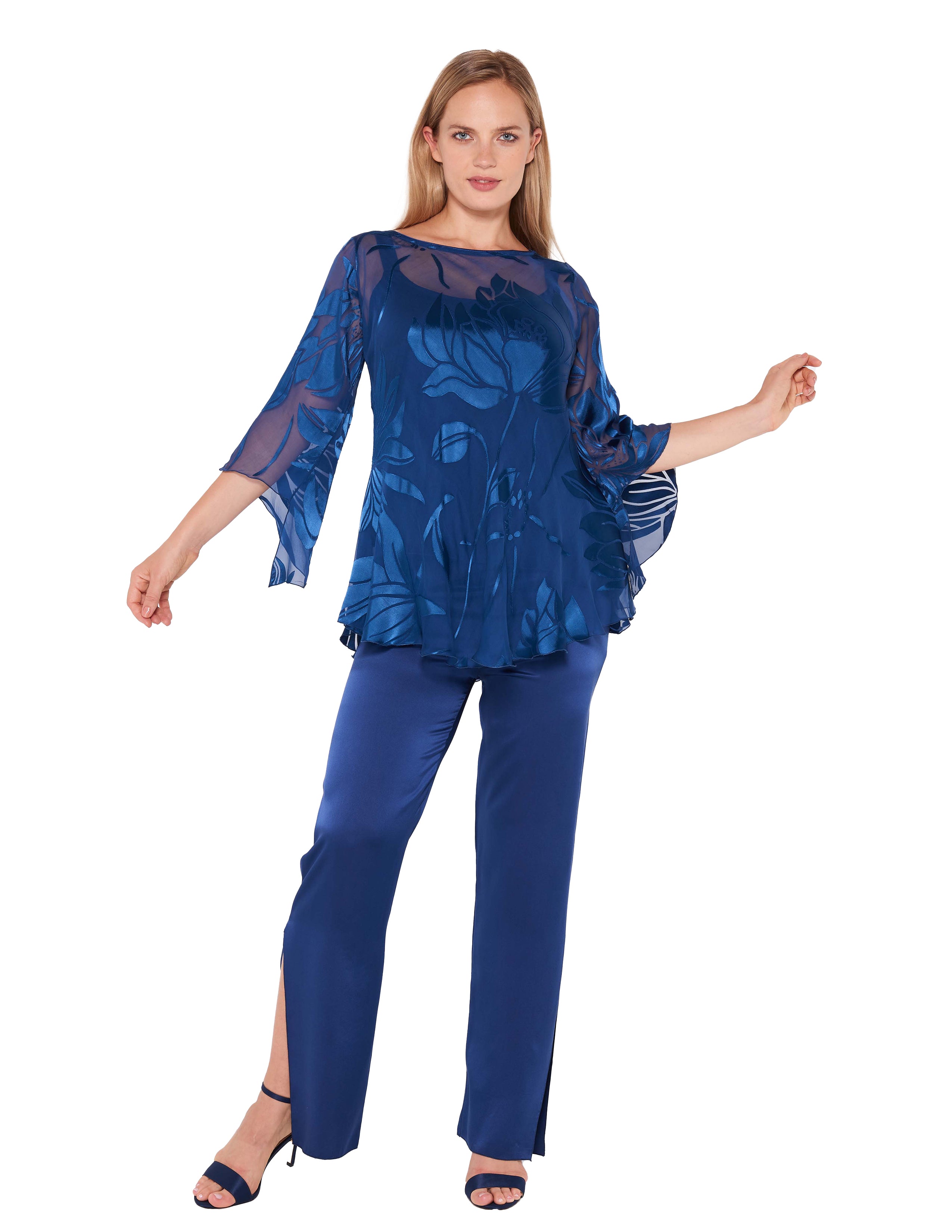 A woman models the Sara Mique Evening Wear Silk Devore Bias Blouse with Silk Liner Cami and Charmeuse Narrow Split Pant, featuring a sheer indigo floral top and matching split-hem pants, smiling gently with arms slightly raised.