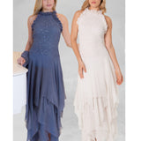 Two women with light hair stand against a plain background in Sara Mique Evening Wear: one in a navy Ultra Feminine Hanky Halter With Ruffles (D1500SCL/Stole2), the other in an off-white high-neck, sleeveless gown with tiered, flowing skirt.