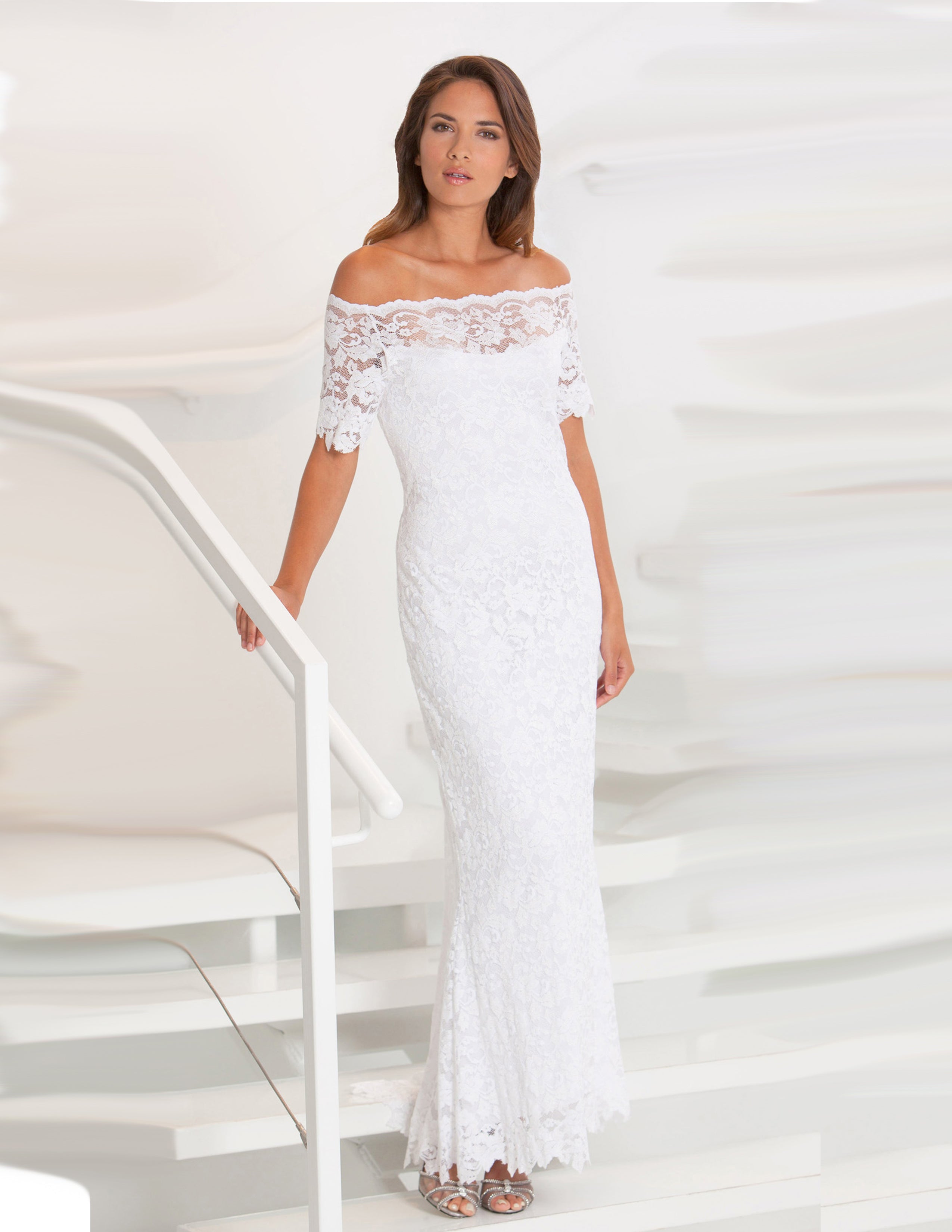 Woman standing in a white lace dress on a white staircase.