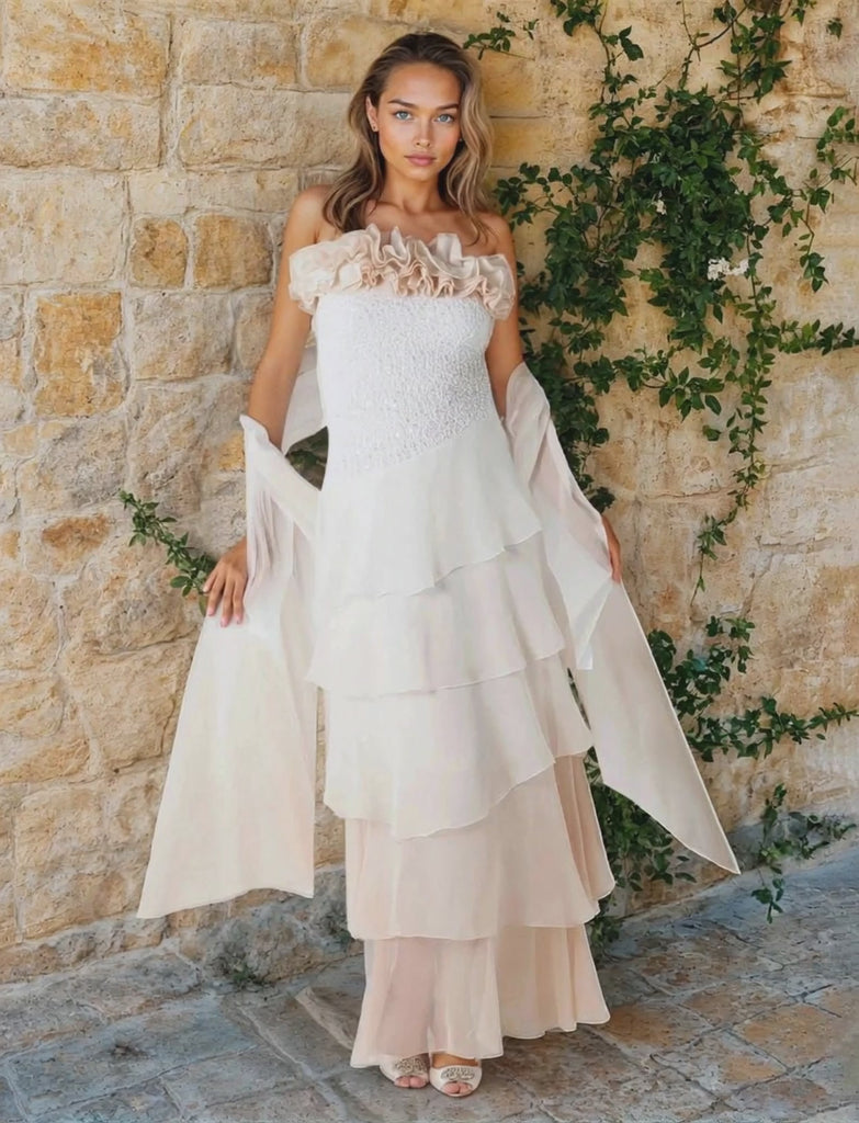 Woman wearing a strapless dress with a  sequin bodice and a silk stole against a stone background with greenery