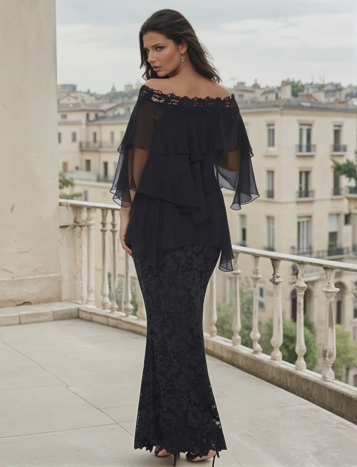 Woman wearing an off the shoulder black lace and plisse blouse with a long lace mermaid skirt on a balcony