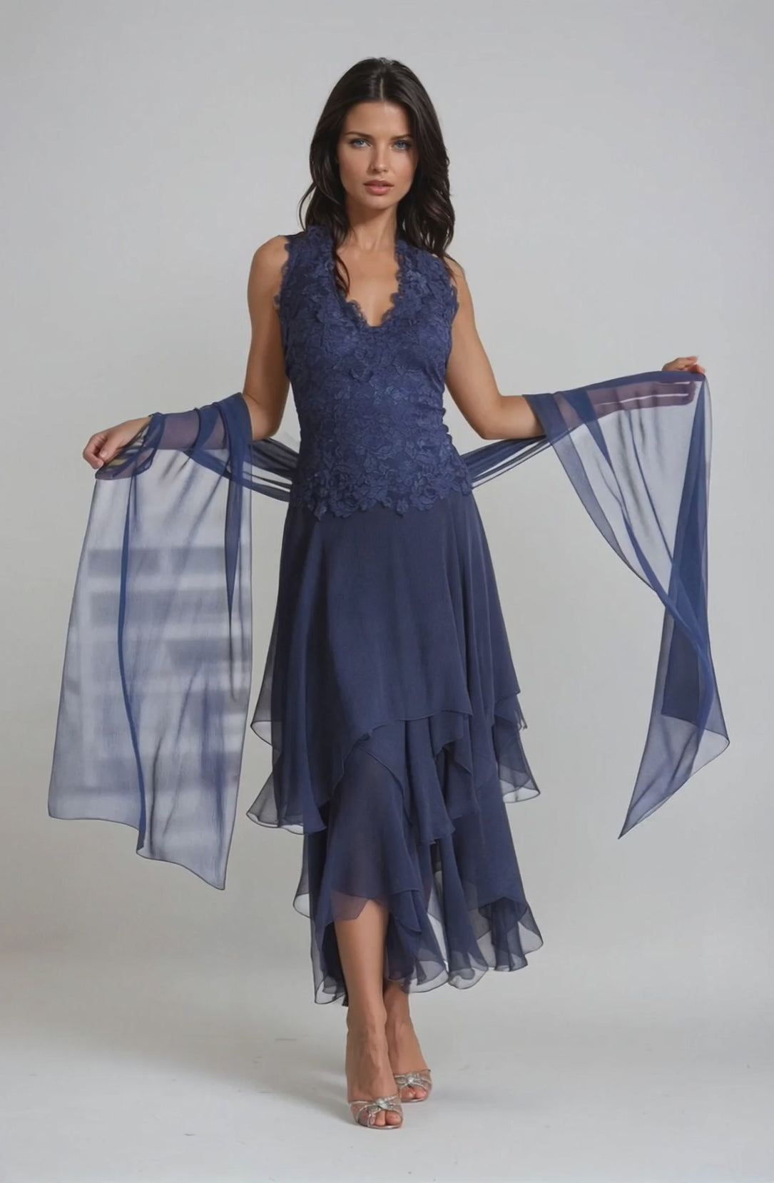 Woman wearing a blue halter top dress with silk layered bottom against a light gray wall