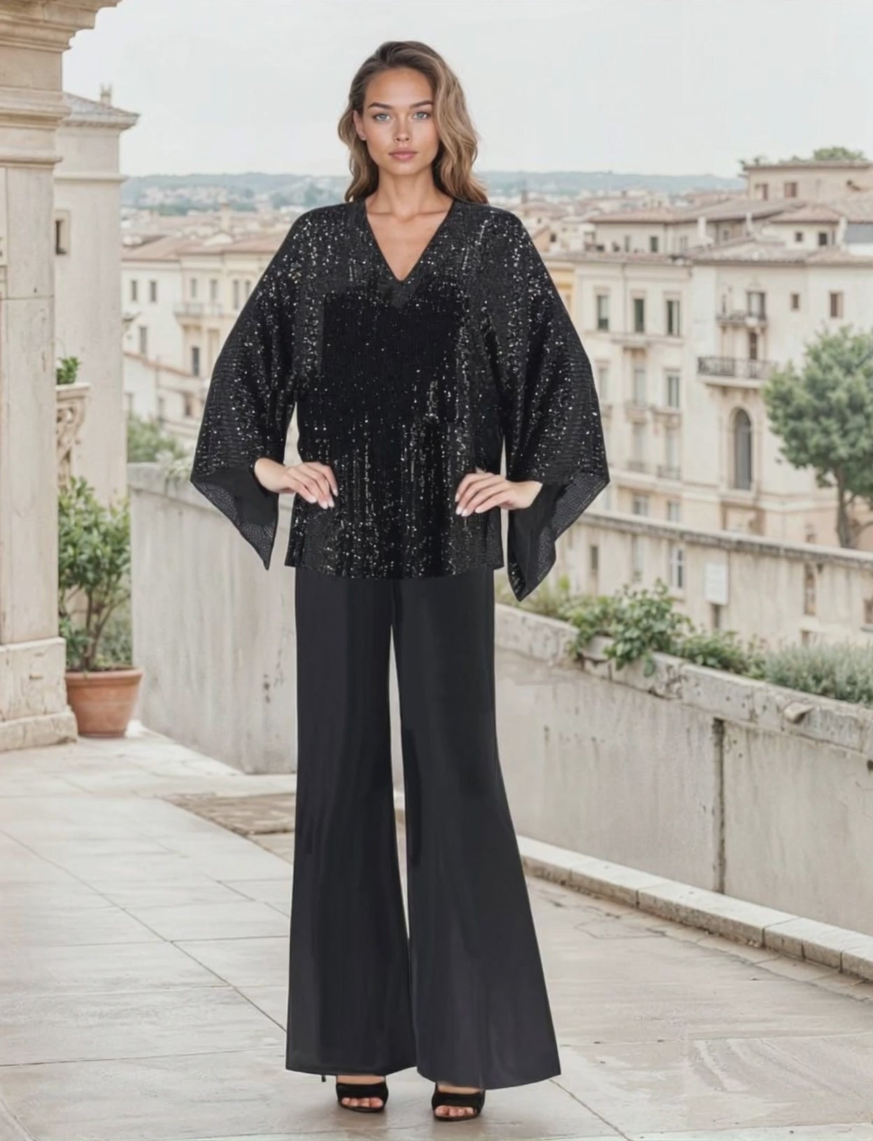 Woman in black seuin pant set standing on a city-scape balcony