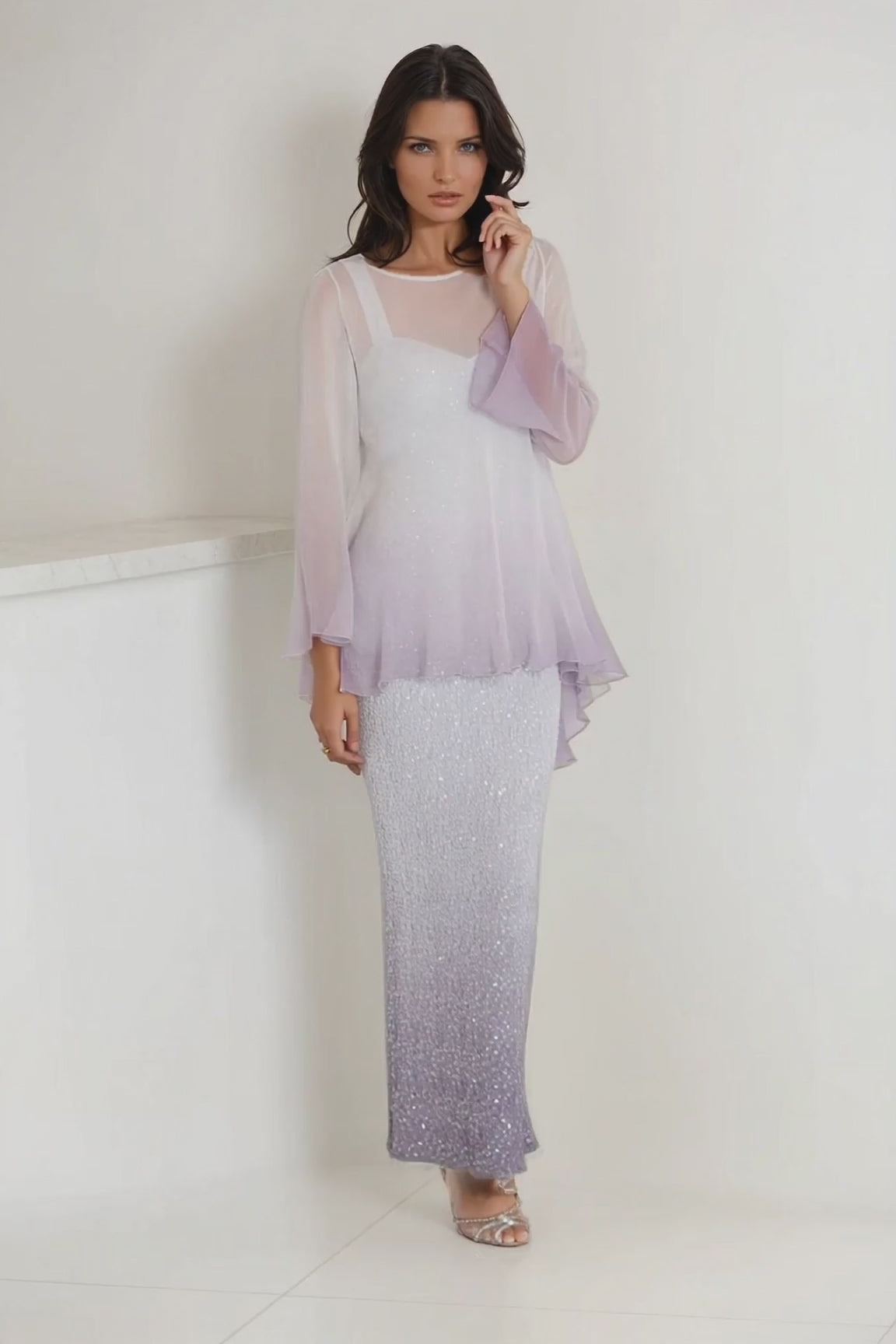 Women wearing a long gray sequin dress with silk tunic overlay on a light gray wall