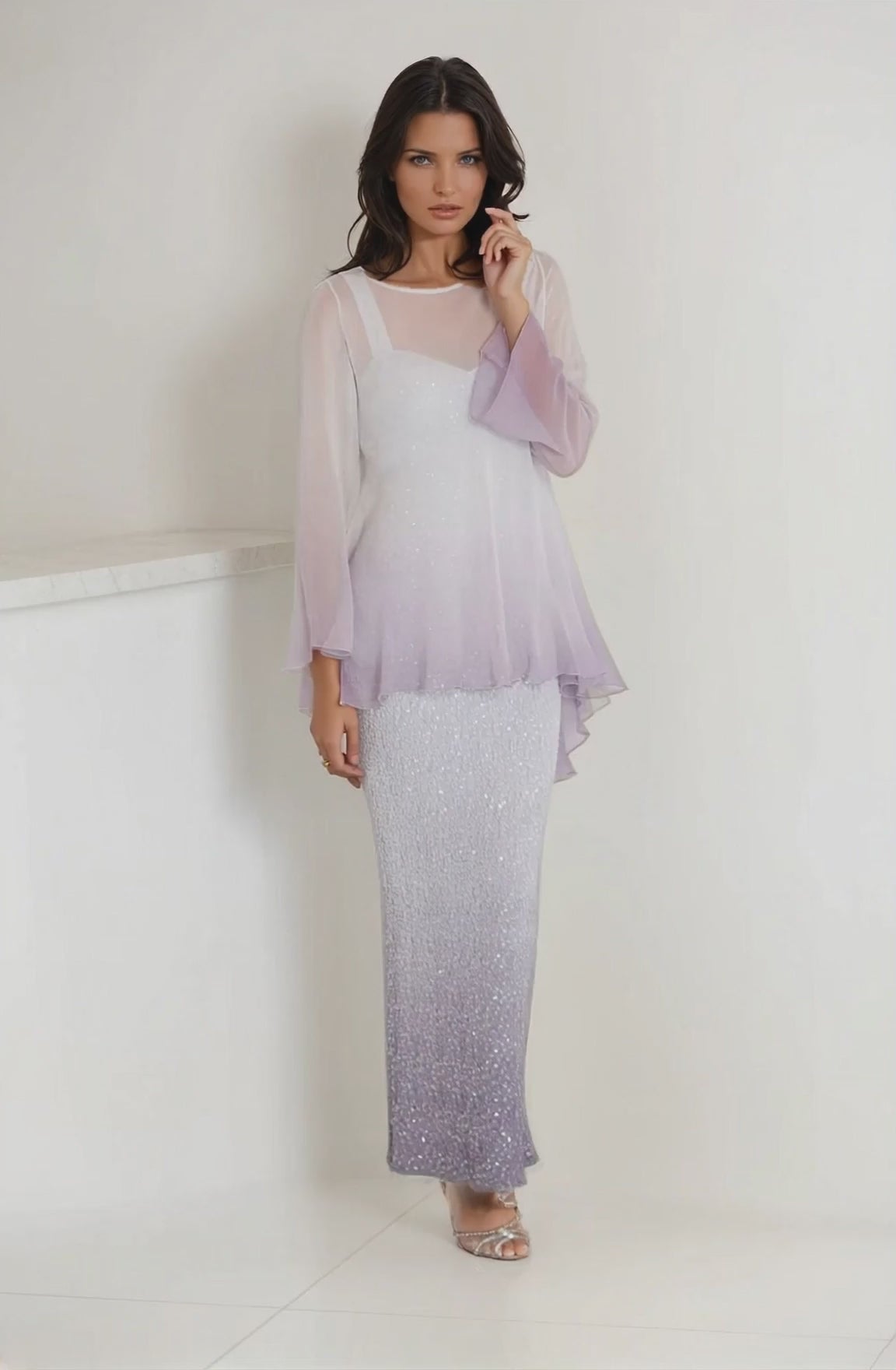 Women wearing a long gray sequin dress with silk tunic overlay on a light gray wall
