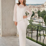 Woman in a white outfit standing on a balcony with a cityscape in the background